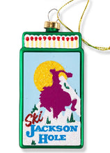 Load image into Gallery viewer, Decorative glass matchbook ornament featuring a skiing cowboy design and Jackson Hole text