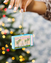 Load image into Gallery viewer, Hand holding a Palm Beach themed matchbox Christmas ornament featuring palm trees and landmark