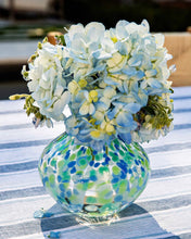 Load image into Gallery viewer, Round glass vase with blue and green speckles holding light blue hydrangeas on striped cloth