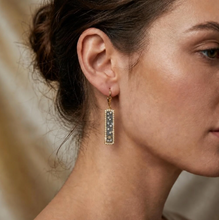 Load image into Gallery viewer, Woman wearing Tat2 Gold Soleil ID Earrings featuring rectangular drop pendants with floral details
