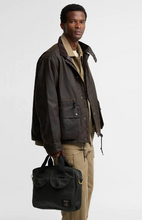 Load image into Gallery viewer, Barbour black waxed cotton laptop bag with dual flap pockets held by male model