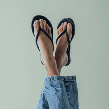 Load image into Gallery viewer, Person wearing Solei Sea Vivie flip flops with slim straps, legs raised in denim shorts