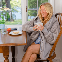 Load image into Gallery viewer, Woman wearing a cozy faux fur cardigan, sitting at a breakfast table holding a mug