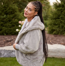 Load image into Gallery viewer, Woman wearing a hooded faux fur oversized cardigan, posing outdoors in a garden setting