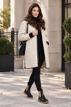 Load image into Gallery viewer, Woman wearing a quilted longline puffer coat with black trim, styled with boots and bag