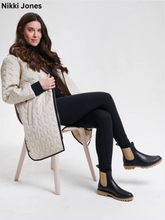 Load image into Gallery viewer, Woman seated in chair wearing quilted long coat with black leggings and Chelsea boots