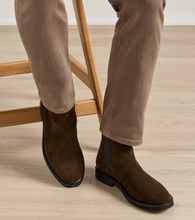 Load image into Gallery viewer, Person seated wearing suede Chelsea boots with elastic side panels and leather sole