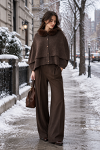 Load image into Gallery viewer, Woman wearing a layered wool poncho with fur collar, styled with wide-leg trousers on a snowy city street