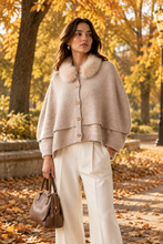 Load image into Gallery viewer, Woman wearing a layered wool poncho with fur collar detail and gold buttons, styled with wide-leg trousers and leather handba