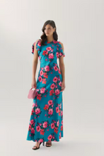 Load image into Gallery viewer, Woman wearing a floral maxi dress with flutter sleeves, holding a small handbag