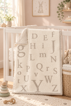 Load image into Gallery viewer, Soft plush alphabet letter blanket draped over a white baby crib in a nursery