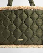 Load image into Gallery viewer, Close-up detail of Barbour quilted tote bag with sherpa trim and gold logo badge