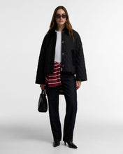 Load image into Gallery viewer, Model wearing a black diamond-quilted jacket with gold buttons over jeans and striped shirt