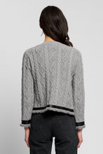 Load image into Gallery viewer, Back view of a cable-knit cardigan with fringe hem and black satin trim details