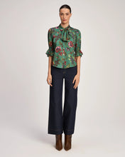Load image into Gallery viewer, Model wearing green floral bow-neck blouse with ruffled sleeves paired with wide-leg dark jeans