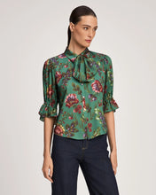 Load image into Gallery viewer, Model wearing a green floral bow-neck blouse with puffed sleeves and ruffled cuffs