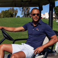 Load image into Gallery viewer, Man wearing navy Auburn polo shirt seated in golf cart on sunny golf course