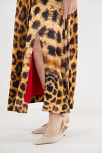 Load image into Gallery viewer, Close-up detail of leopard print maxi skirt with side slit and red lining, styled with nude heels