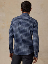 Load image into Gallery viewer, Back view of man wearing a long-sleeve navy plaid button-up shirt with dark trousers
