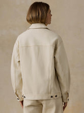 Load image into Gallery viewer, Back view of a woman wearing an oversized cream denim trucker jacket with snap-button hem