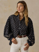 Load image into Gallery viewer, Model wearing a loose-fitting navy floral button-up blouse with voluminous sleeves and white jeans