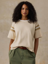 Load image into Gallery viewer, Woman wearing an oversized cream jersey tee with sporty striped sleeves and green trousers