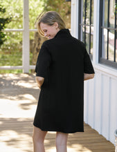 Load image into Gallery viewer, Woman wearing a black short sleeve mini dress with turtleneck, viewed from behind on a porch
