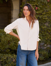 Load image into Gallery viewer, Woman wearing a relaxed cream button-up shirt with chest pocket paired with wide-leg jeans outdoors