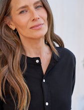 Load image into Gallery viewer, Woman wearing a black button-front blouse with white buttons and band collar, close-up detail shot