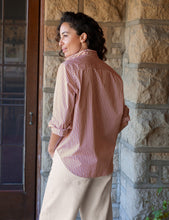 Load image into Gallery viewer, Woman wearing striped button-up shirt with rolled sleeves, shown from behind near stone building