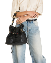 Load image into Gallery viewer, Model wearing light jeans holds a black leather drawstring bucket bag with gold hardware