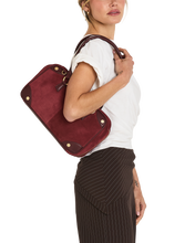 Load image into Gallery viewer, Model wearing white tee and pinstripe trousers carries a burgundy suede shoulder bag with gold hardware