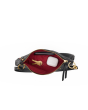 Load image into Gallery viewer, Overhead view of open black leather crossbody bag with red interior, keys, and AirPods case