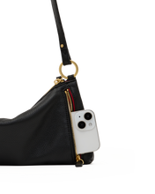 Load image into Gallery viewer, Close-up detail of black leather shoulder bag showing gold zipper and phone pocket with white smartphone