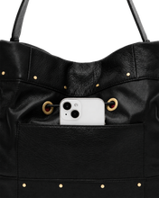 Load image into Gallery viewer, Close-up detail of black leather tote bag exterior pocket holding a white smartphone