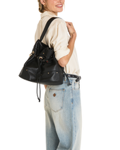 Load image into Gallery viewer, Model wearing black leather drawstring bucket bag with gold hardware over shoulder