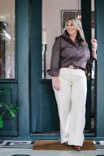 Load image into Gallery viewer, Woman wearing a mocha satin button-up ruffle shirt with wide-leg cream trousers standing in a doorway
