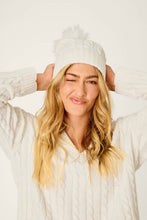 Load image into Gallery viewer, Model wearing ivory cable-knit beanie with pom-pom, hands raised to head, playful expression
