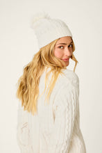 Load image into Gallery viewer, Model wearing ivory cable-knit beanie with pom-pom, shown from behind glancing over shoulder