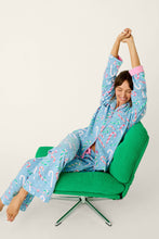 Load image into Gallery viewer, Woman stretching arms overhead wearing candy cane print pajama set while seated in green chair