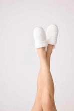 Load image into Gallery viewer, Legs raised in air wearing cozy ivory cable-knit slide slippers with ribbed cuff