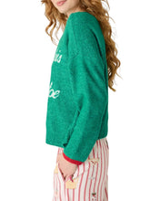 Load image into Gallery viewer, Side view of woman wearing green holiday sweater with cursive text and striped pants
