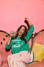 Load image into Gallery viewer, Model wearing green Martinis and Mistletoe holiday sweatshirt with striped pants, seated on pink sofa