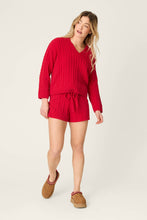 Load image into Gallery viewer, Model wearing red cable knit V-neck sweater with matching drawstring shorts and tan slippers