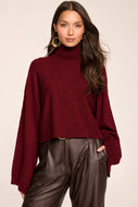 Model wearing a cropped turtleneck sweater with wide sleeves paired with leather trousers