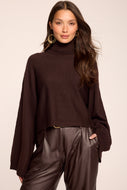 Model wearing a dark brown turtleneck cropped sweater with wide sleeves and ribbed cuffs