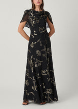 Load image into Gallery viewer, Model wearing a floor-length black gown with gold metallic floral embroidery and cape sleeves