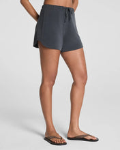 Load image into Gallery viewer, Model wearing dark gray elastic-waist drawstring shorts with side pockets and flip flops