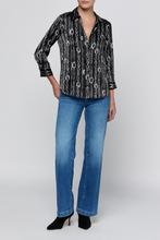 Load image into Gallery viewer, Model wearing a black and silver chain-print satin blouse with three-quarter sleeves and blue jeans